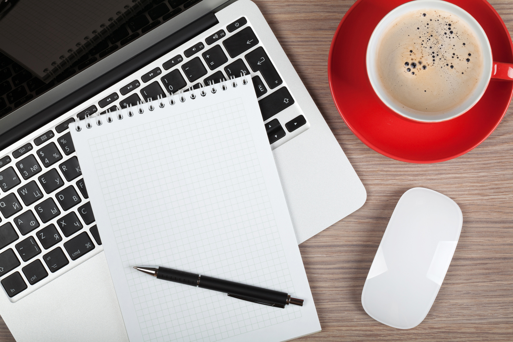 Blank notepad over laptop and coffee cup on office wooden table